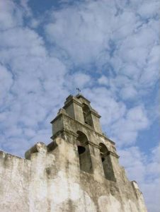 Bell tower of Mission San Juan church with clouds behind it.